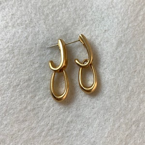 May include: A pair of gold-toned earrings with a double-loop design. The earrings are made of a smooth, shiny metal.