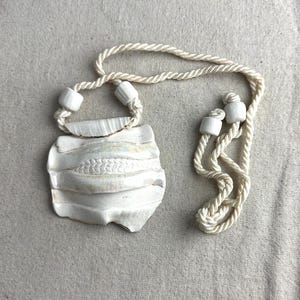 May include: A white ceramic necklace with a textured, shell-like pendant and a white rope chain.