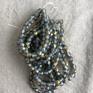 May include: A strand of gray and gold glass beads with a faceted finish. The beads are strung on a clear thread.