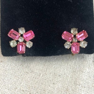 May include: A pair of pink and clear rhinestone earrings with a flower design.