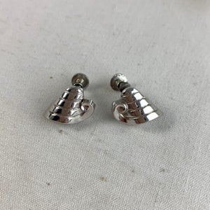 May include: A pair of silver tone clip-on earrings with a geometric design. The earrings are shaped like a curved triangle with a series of ridges.