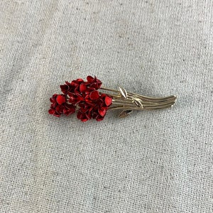 May include: A red and gold brooch featuring a bouquet of red flowers with a silver stem and leaves.