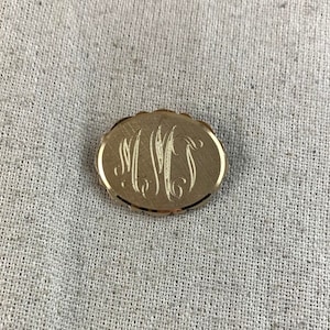 May include: A gold oval-shaped brooch with a monogram of the letters "MWS" engraved in the center.