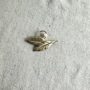 May include: A silver-toned leaf-shaped brooch with a small white pearl accent.