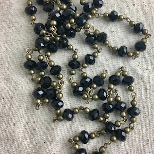 May include: A long necklace featuring alternating black faceted crystal beads and small round antique brass-toned metal beads connected by thin metal links. The beads are arranged in a repeating pattern along the entire length of the chain.