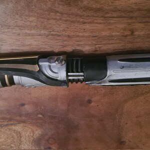 May include: A black, silver, and gold lightsaber prop with a textured handle and a black blade.
