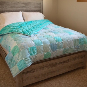 May include: A blue and white patchwork quilt with a tied knot design on a wooden bed frame.