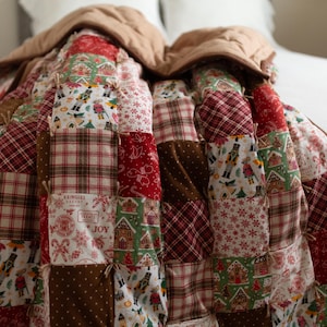 May include: A patchwork quilt featuring a variety of holiday-themed fabric squares in red, green, white, and brown. The patterns include nutcrackers, gingerbread houses, candy canes, and plaid designs, with visible hand-tied knots at each corner.