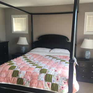 May include: A black four-poster bed with a pink and green patchwork quilt. The bed has a white headboard and footboard. There are two bedside tables with lamps on them.