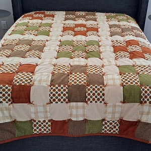 May include: A patchwork quilt with squares of brown, green, and orange fabric. The quilt is made with a variety of patterns and textures.