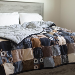 May include: A patchwork quilt with a variety of fabrics in shades of blue, brown, and cream, featuring sheep motifs. The quilt is on a bed with white pillows and a gray headboard. The quilt's dimensions are approximately 80 inches by 90 inches.
