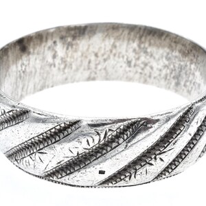 Könnte beinhalten: Ein silberfarbenes Armreif-Armband mit geätzten diagonalen Linien und detaillierten Mustern. Das breite Band hat ein strukturiertes Aussehen mit leicht angelaufenem Finish. Das Schmuckstück ist vor einem weißen Hintergrund platziert.