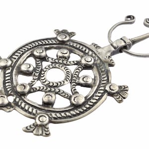 May include: A silver circular brooch with an intricate design of interwoven circles and dots. The brooch has a pin and catch on the side.