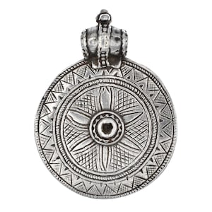 May include: A circular silver-toned metal pendant featuring an intricate engraved floral pattern at the center, surrounded by a geometric border of triangles and cross-hatching. The piece includes a decorative bail at the top for suspension.