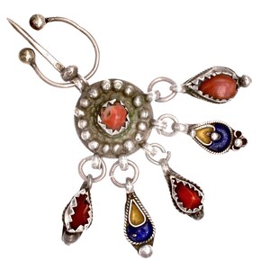 May include: A silver-toned brooch with a central coral-colored stone surrounded by a beaded design. Dangling from the center are teardrop-shaped pendants with red, yellow, and blue stones. The brooch has a pin closure.