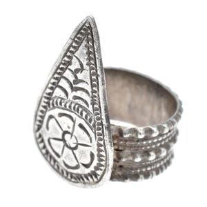Può includere: Anello d'argento con una grande faccia a forma di goccia. La faccia presenta un motivo floreale in rilievo ed è affiancata da una fascia strutturata. L'anello ha un'estetica vintage o antica.