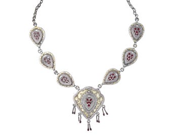 Può includere: Una collana d'argento con un ciondolo a forma di lacrima. Il ciondolo è decorato con una pietra rossa e un'intricata lavorazione in argento. La collana è adornata con ciondoli più piccoli a forma di lacrima, ognuno con una pietra rossa.