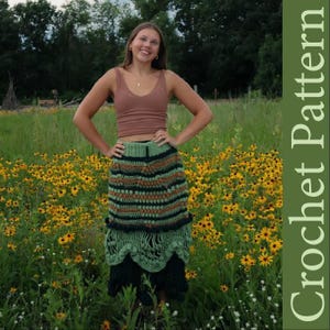 May include: A woman wearing a crochet skirt with green, brown, and black stripes. The skirt has a scalloped hem and is paired with a brown tank top. The background features a field of yellow flowers and green foliage.