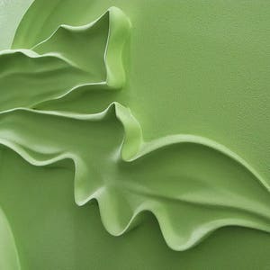 May include: A close-up of a green, three-dimensional, floral design. The design is made of a smooth, textured material and has a flowing, organic shape.