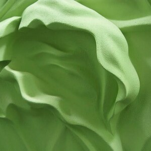 May include: Abstract green fabric with a textured surface and flowing folds.