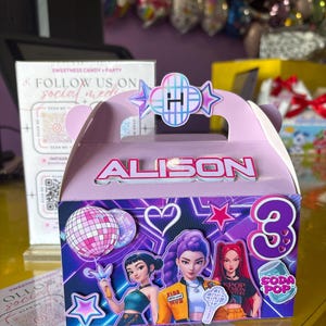 May include: A light purple party favor box with the name "ALISON" in white. The box features illustrations of three cartoon figures, a disco ball, a star, and the number "3". The box also has the text "SODA POP".