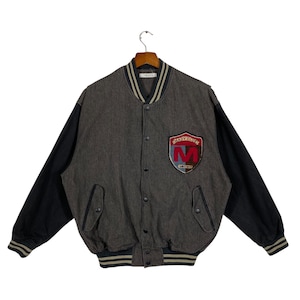 May include: A gray and black varsity jacket with a button-up front. The jacket features black sleeves, a gray body, and a patch on the chest that reads "Mady Club" with an "M" in red. The jacket has a striped collar, cuffs, and hem.