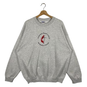 Pode incluir: Camisola de moletom cinza com um logotipo circular que diz "Anderson Street United Methodist Church" com um design de chama vermelha e cruz.