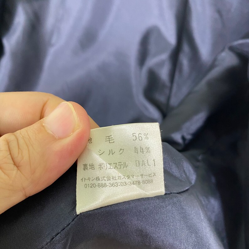 Puede incluir: Una etiqueta de tela blanca con texto negro que detalla la composici&oacute;n de la tela de una prenda. La etiqueta dice: "毛 56% シルク 44% 裏地 ポリエステル DAL1 イトキン株式会社カスタマーサービス 0120-888-363:03-3478-8088"
