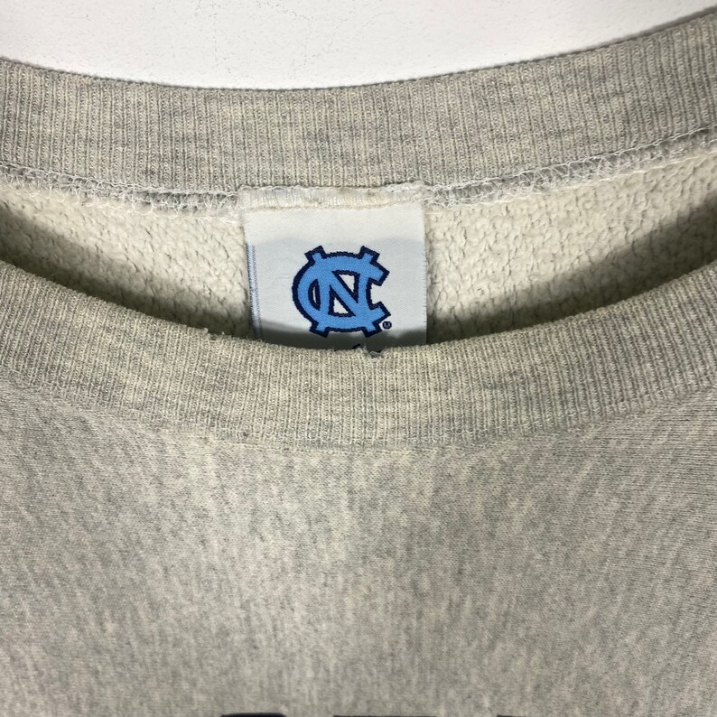 May include: A gray sweatshirt with a blue and white logo of a "C" inside a circle. The logo is on a white tag sewn into the neck of the sweatshirt.