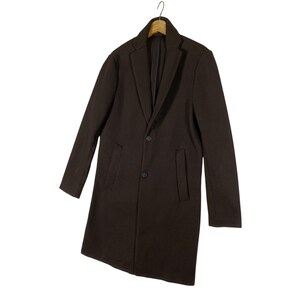 Pu&ograve; includere: Un cappotto lungo marrone a maniche lunghe con una chiusura a bottone singolo e due tasche. Il cappotto ha un orlo leggermente asimmetrico.