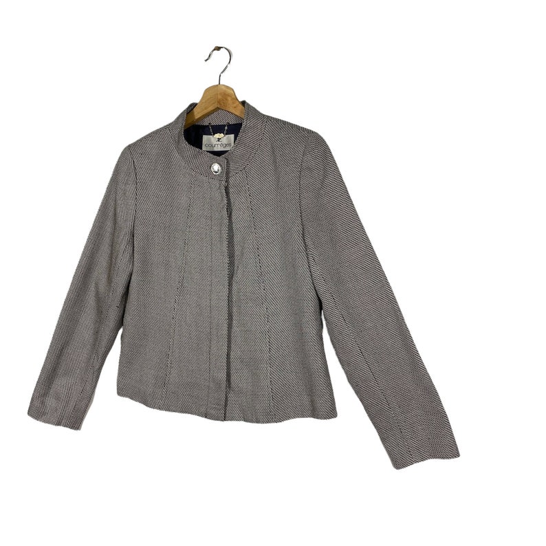 Puede incluir: Una chaqueta de color gris y blanco con un patr&oacute;n, cierre de cremallera y un solo bot&oacute;n en el cuello. La etiqueta de la chaqueta dice "Couture 1992".