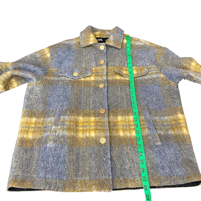 May include: A gray and yellow plaid jacket with gold buttons and two chest pockets. The jacket has a collared neckline and long sleeves. The jacket is measured with a green measuring tape.