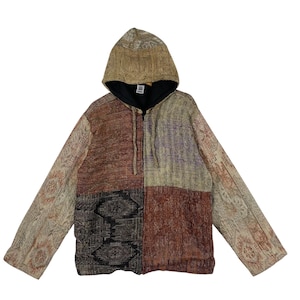 Puede incluir: Una sudadera con capucha de patchwork con cremallera completa y capucha. La chaqueta presenta una variedad de telas en tonos tierra, incluyendo marrón, beige y negro, con patrones intrincados. El forro interior es negro.