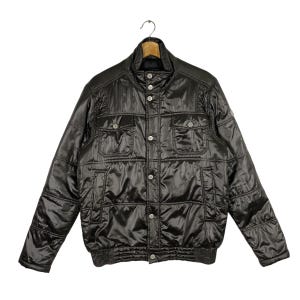 Puede incluir: Una chaqueta acolchada negra con cierre de botones a presión y dos bolsillos de solapa. La chaqueta tiene un dobladillo y puños de canalé.