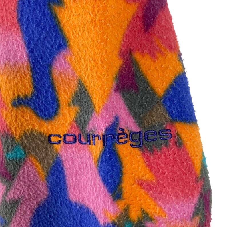 May include: A colorful fleece jacket with a geometric pattern in shades of orange, pink, blue, purple, and green. The jacket has a purple embroidered logo that reads "Courr&egrave;ges".