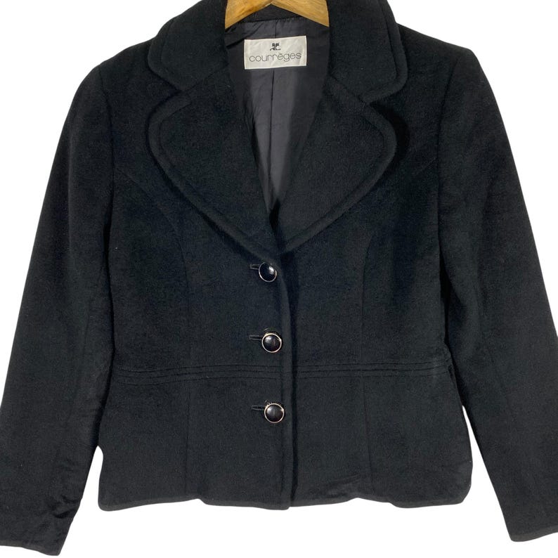 May include: A black wool blazer with a notched collar, three buttons, and a curved pocket detail. The label reads "Courr&egrave;ges".