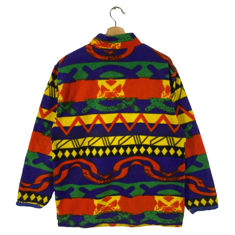 Puede incluir: Una chaqueta de forro polar colorida con un patr&oacute;n geom&eacute;trico en tonos de rojo, amarillo, verde, azul y negro. La chaqueta tiene un cuello alto y una cremallera.