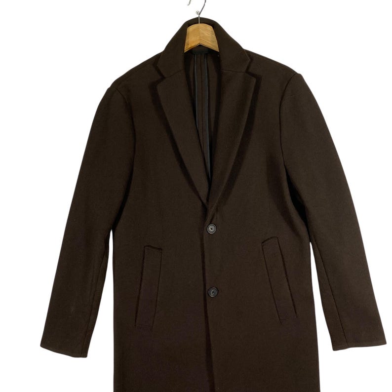 Pu&ograve; includere: Un cappotto marrone a maniche lunghe con chiusura a un solo bottone e due tasche anteriori.