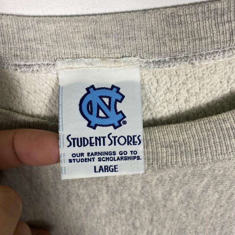May include: A gray sweatshirt with a white tag that says "Student Stores" and has a blue "N" logo. The tag also says "Our earnings go to student scholarships." and "Large".