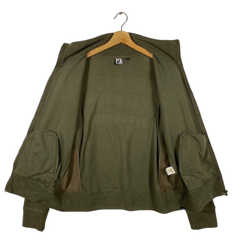 Puede incluir: Sudadera con capucha con cremallera verde oliva con capucha y dos bolsillos delanteros. La chaqueta est&aacute; colgada de una percha de madera. El interior de la chaqueta es visible, mostrando un forro verde oliva a juego y una etiqueta con texto.