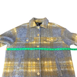 May include: A button-down jacket in a blue and yellow plaid pattern. The jacket has two chest pockets and gold-colored buttons. The jacket is being measured with a green measuring tape.