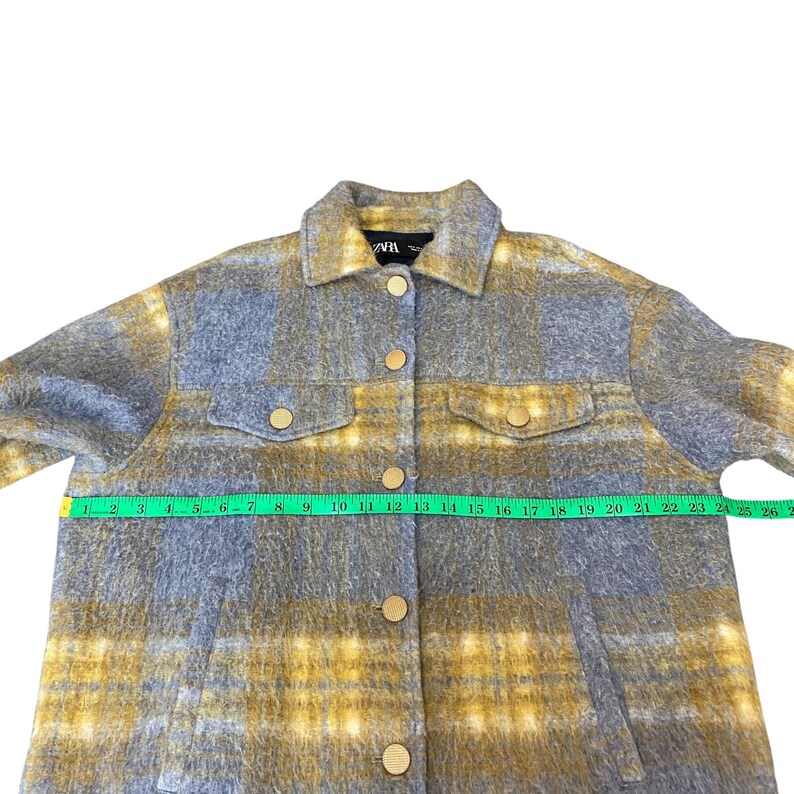 May include: A button-down jacket in a blue and yellow plaid pattern. The jacket has two chest pockets and gold-colored buttons. The jacket is being measured with a green measuring tape.