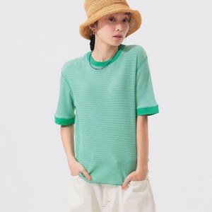 May include: A person wearing a straw hat and a green and white striped t-shirt with green trim. The person is also wearing white trousers. The outfit is casual and suitable for warm weather.
