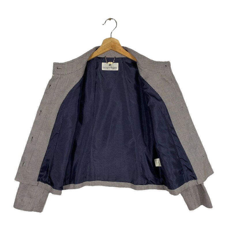 Puede incluir: Una chaqueta de cuadros marr&oacute;n y blanco con forro azul marino. La chaqueta tiene una etiqueta que dice "Courr&egrave;ges" en el interior.