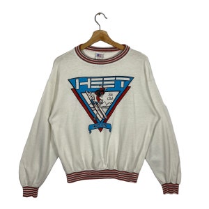 May include: White sweatshirt with a red and blue striped collar and cuffs. The front of the sweatshirt features a blue and red graphic of a skier in a triangle with the text "HEET Ski Club" and "May 1987".