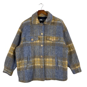 May include: A blue, yellow, and gray plaid jacket with a collared neckline and button-down front. The jacket has two chest pockets and two side pockets. The brand name "ZARA" is visible on the label.