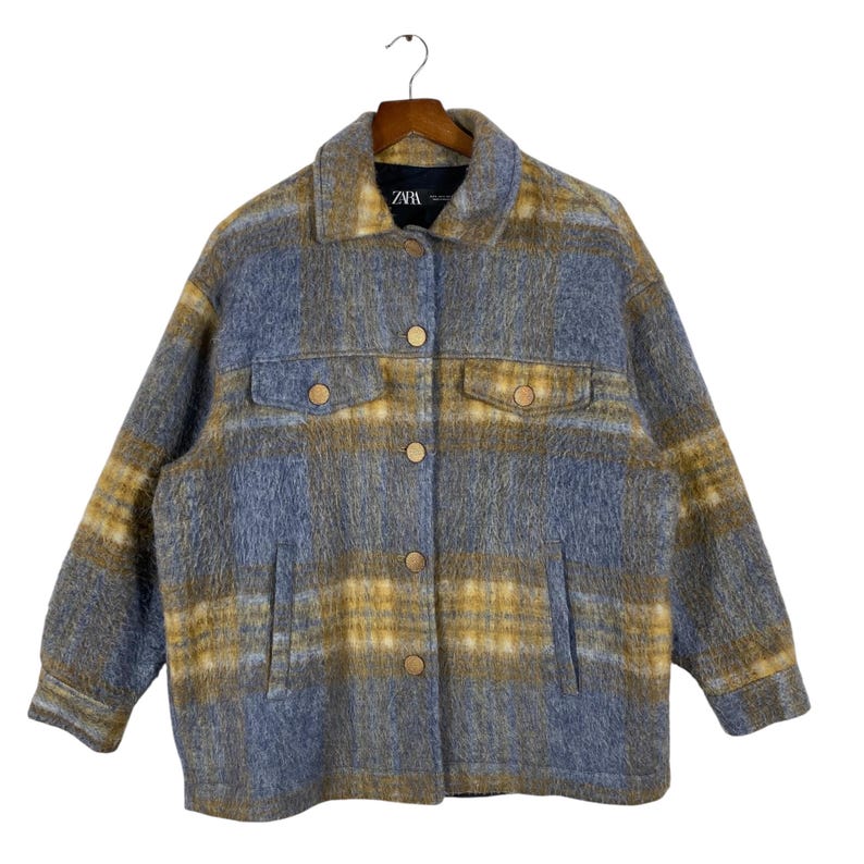 May include: A blue, yellow, and gray plaid jacket with a collared neckline and button-down front. The jacket has two chest pockets and two side pockets. The brand name "ZARA" is visible on the label.