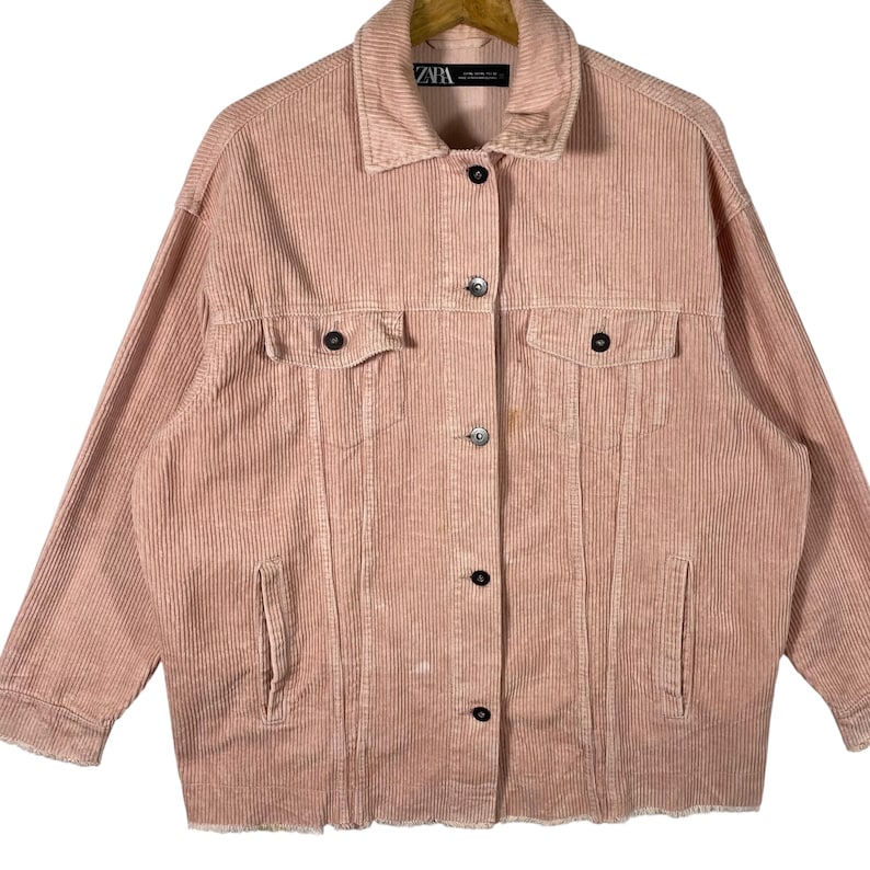 K&ouml;nnte beinhalten: Staubrosa Cordjacke mit Knopfleiste, zwei Brusttaschen und zwei Seitentaschen. Die Jacke hat einen klassischen Kragen und lange &Auml;rmel. Der Saum ist ausgefranst. Das Markenlabel "ZARA" ist sichtbar.