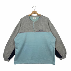 Puede incluir: Una sudadera de manga larga gris y azul claro con cuello de botones y la palabra "LACOSTE" bordada en la parte delantera.