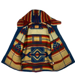 Könnte beinhalten: Eine blaue Jeansjacke mit einem bunten südwestlichen Musterfutter. Das Futter zeigt geometrische Formen und Streifen in Rot, Gelb, Blau und Grün.